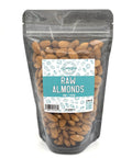 A black zippered bag filled with raw almonds with a clear front and a teal and white label on the front