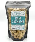 A black zippered bag filled with raw cashews with a clear front and a teal and white label on the front