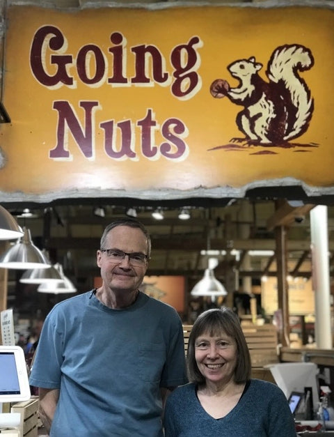 A couple standing in front of a yellow sign for their booth that says Going Nuts with a squirrel logo.
